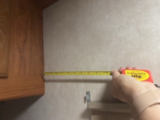 Shayne measuring the space beside a wooden cabinet in Big Bob for a future bookshelf.